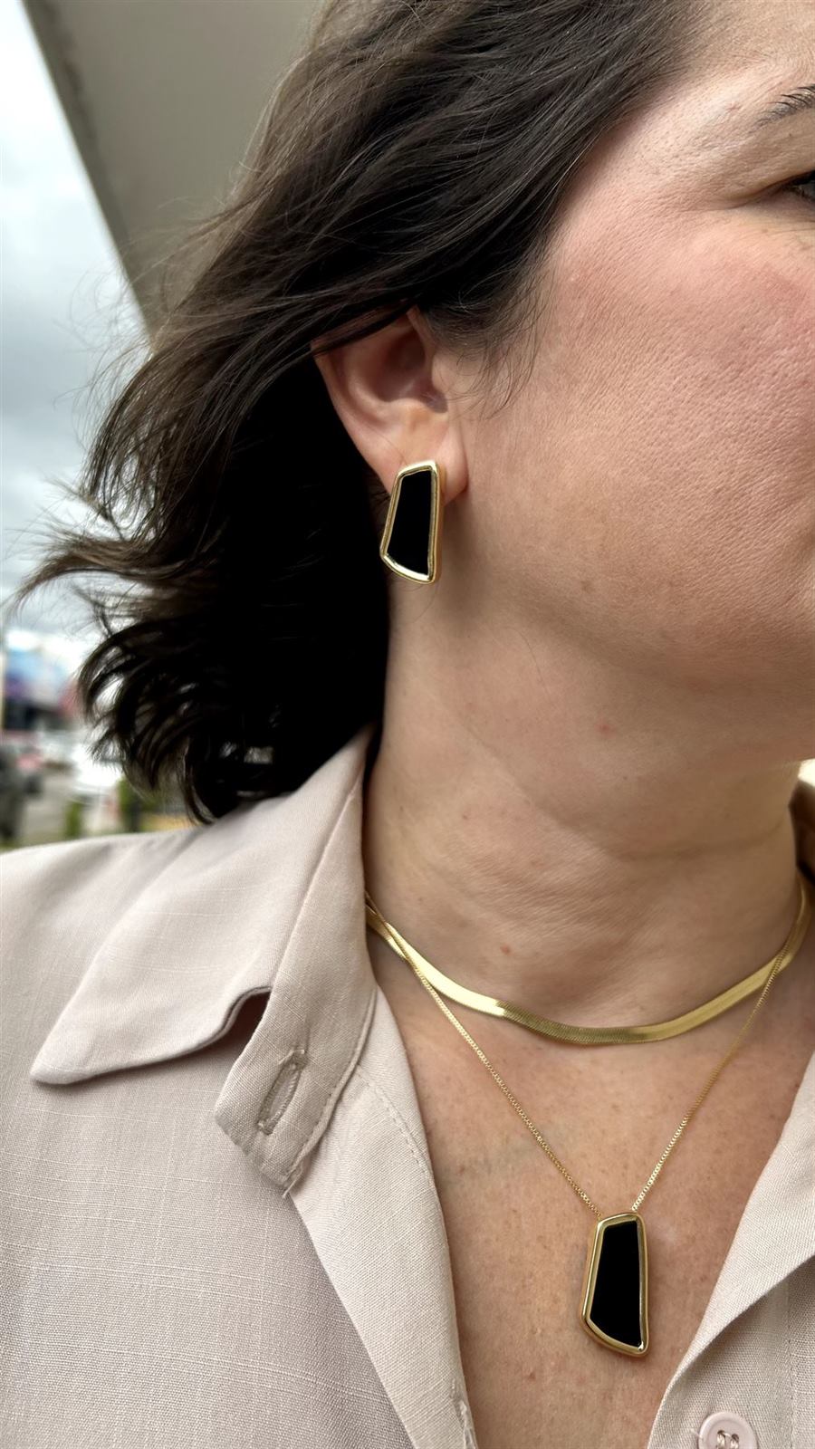 Mulher usando conjunto de colar e brinco dourado com pedra escura
