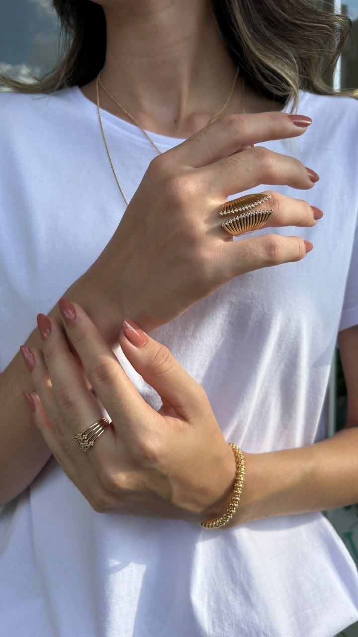 Mulher usando anéis e pulseira dourada em composição editorial